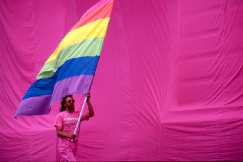 Gilbert Baker holds the rainbow flag against a pink backdrop