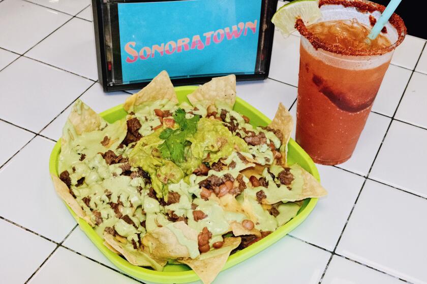 Costilla (steak) nachos on a green tray next to a red michelada and napkin holder that reads "SONORATOWN" at the cantina.