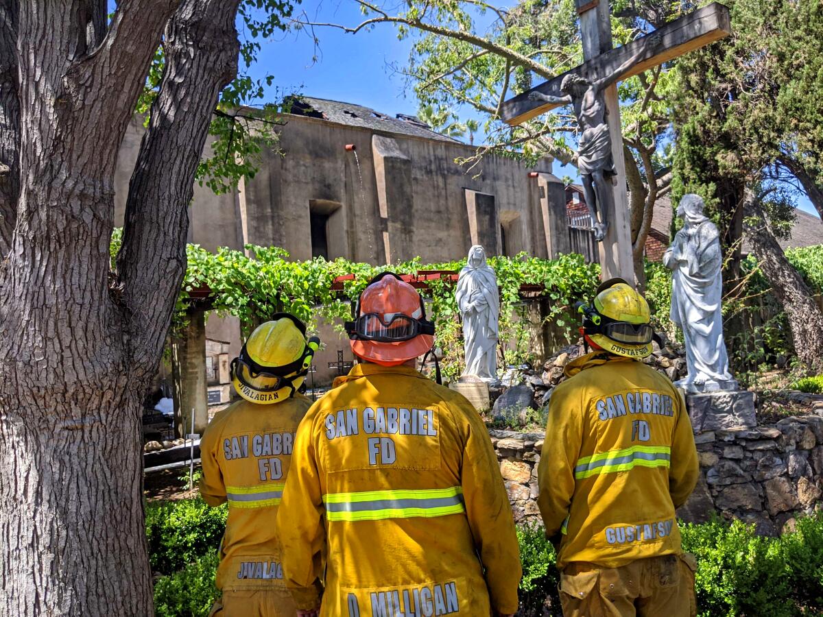 Firefighters in yellow uniforms stand before the San Gabriel Mission.