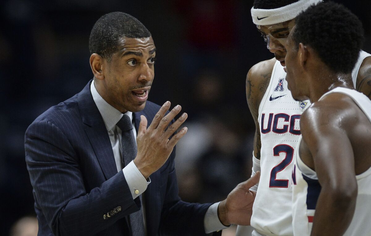 FILE - Connecticut head coach Kevin Ollie, left, talks with Connecticut's Terry Larrier and Christian Vital, right, during an NCAA college basketball game, Wednesday, Feb. 7, 2018, in Storrs, Conn. An independent arbiter has ruled that UConn improperly fired former men's basketball coach Kevin Ollie and must pay him more than $11 million, Ollie's lawyer said Thursday, Jan. 20, 2022. (AP Photo/Jessica Hill, File)