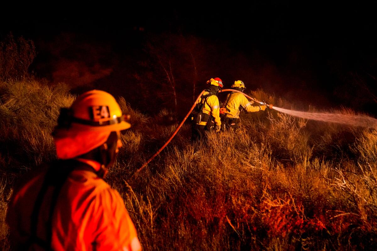 Firefighters battle the Bond Fire, started by a structure fire that extended into nearby vegetation.