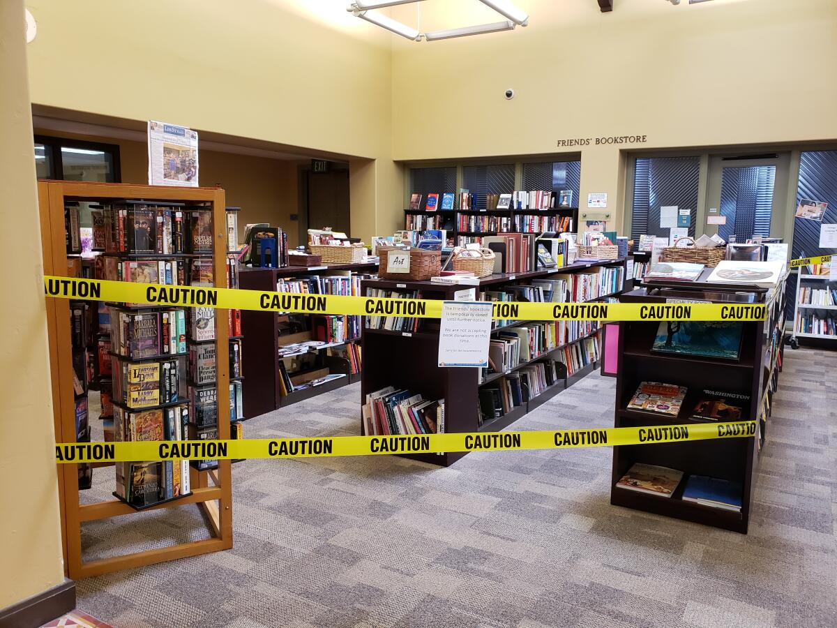 Caution tape is spread across bookshelves at the La Jolla/Riford Library to prevent crowding.