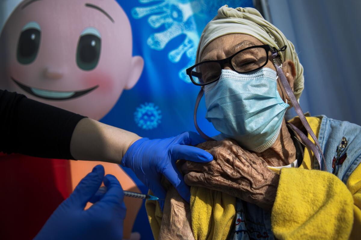 A masked woman wearing glasses receives a needle jab in the arm 