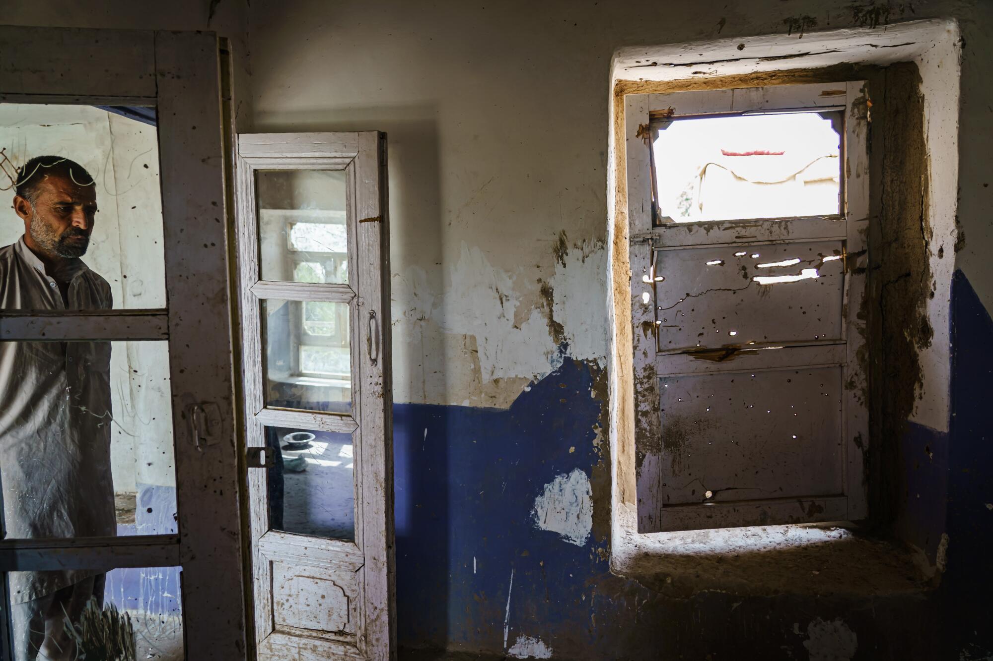 A man stands inside a home with holes in the walls and doors.