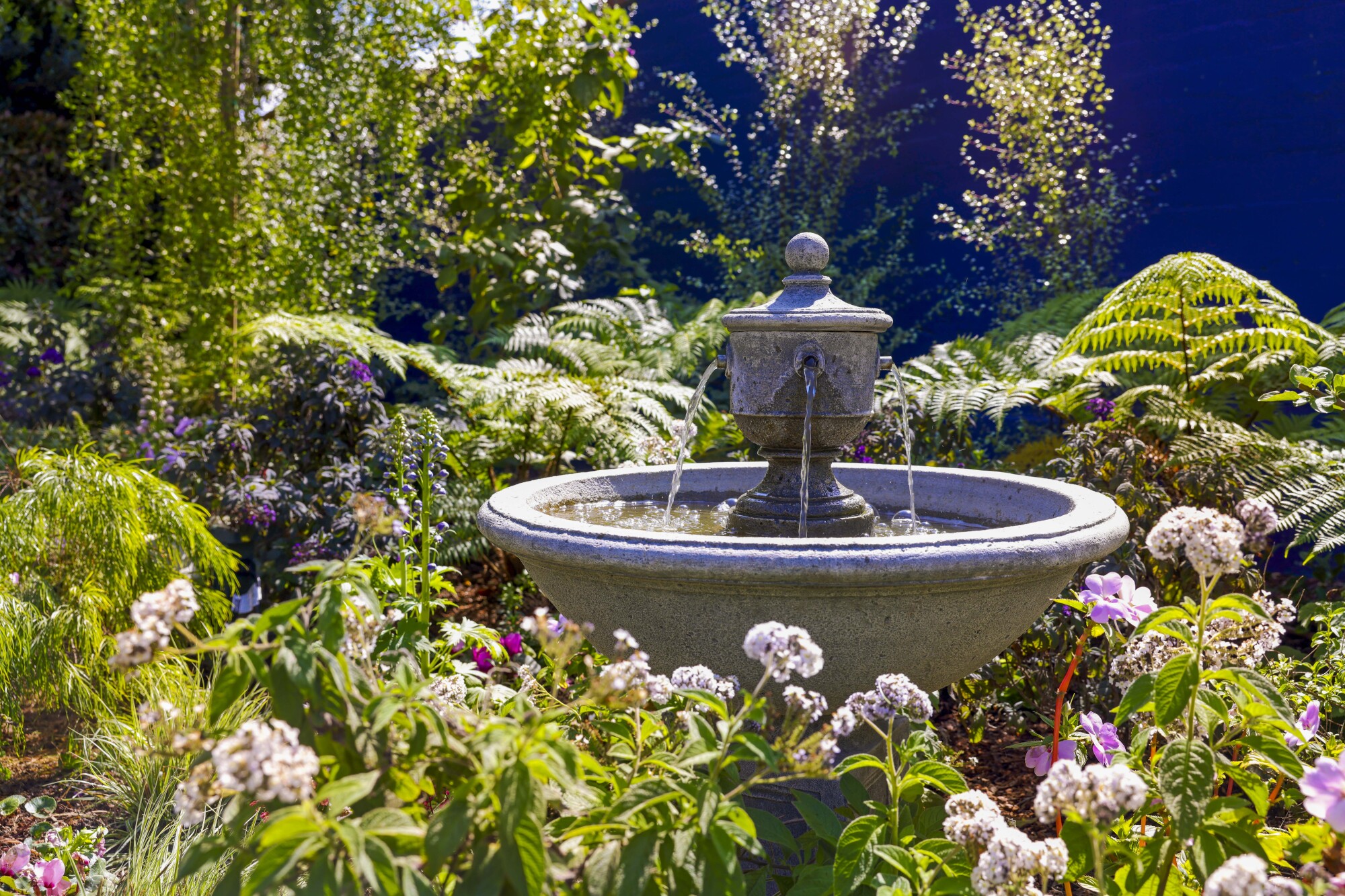 Water flows from a stone fountain surrounded by flowers.