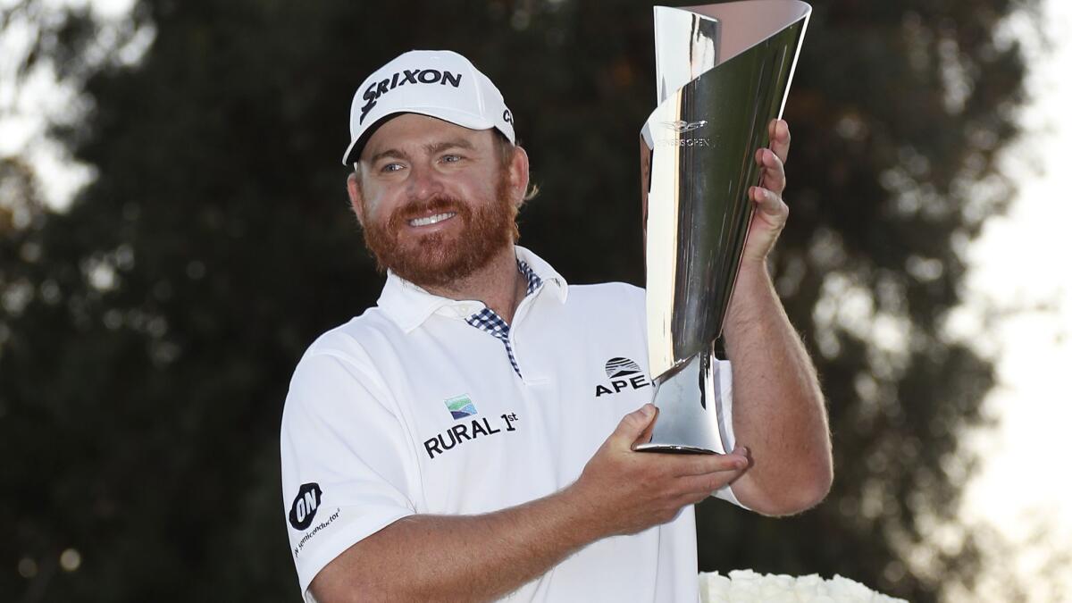 J.B. Holmes holds up the winner's trophy on the 18th green at the conclusion of the Genesis Open on Sunday at Riviera Country Club.