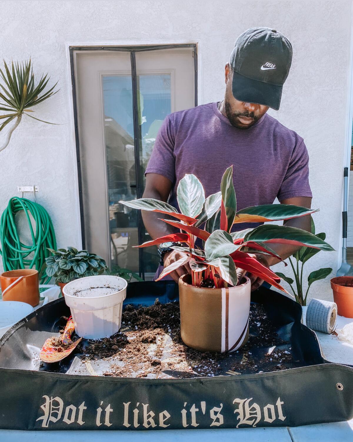 A man looks caringly at a plant that sits atop a gardening mat with the words "Pot It Like It's Hot" printed on it.