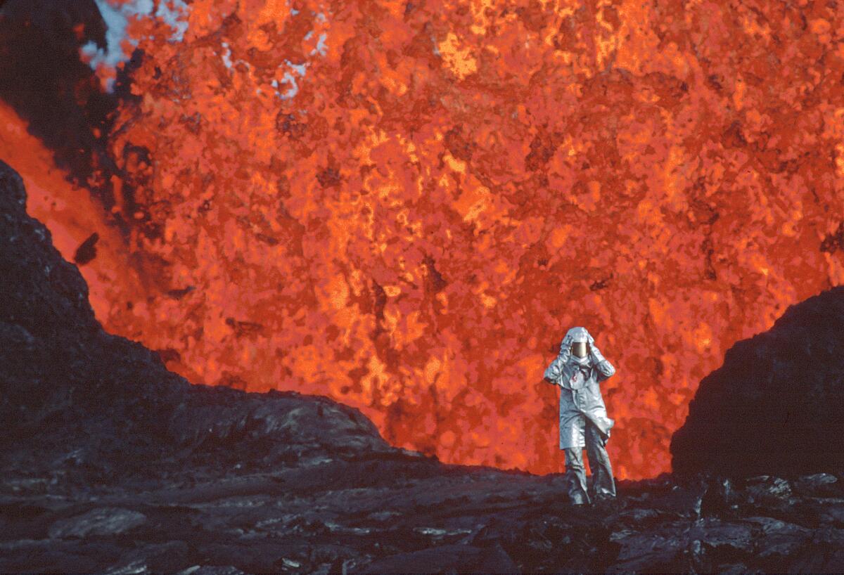 This image released by National Geographic shows Katia Krafft wearing an aluminized suit as she stands near lava burst at Krafla Volcano, Iceland, in a scene from the documentary "Fire of Love." (National Geographic via AP)