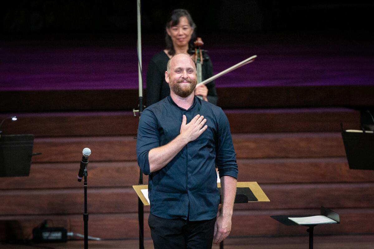 Christopher Rountree, wearing a blue shirt, places his hand over his chest as he acknowledges the audience
