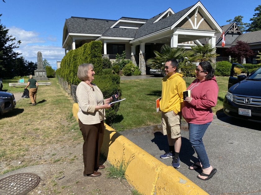 A woman standing on the U.S. side of a low yellow barrier talks with a man and woman standing a few feet away in Canada.