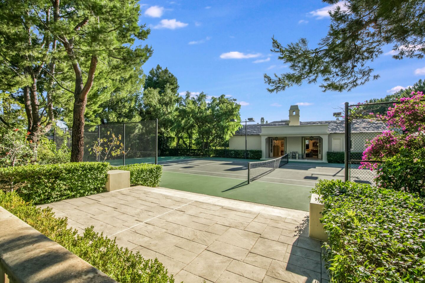 The tennis court is next to the home and greenery.