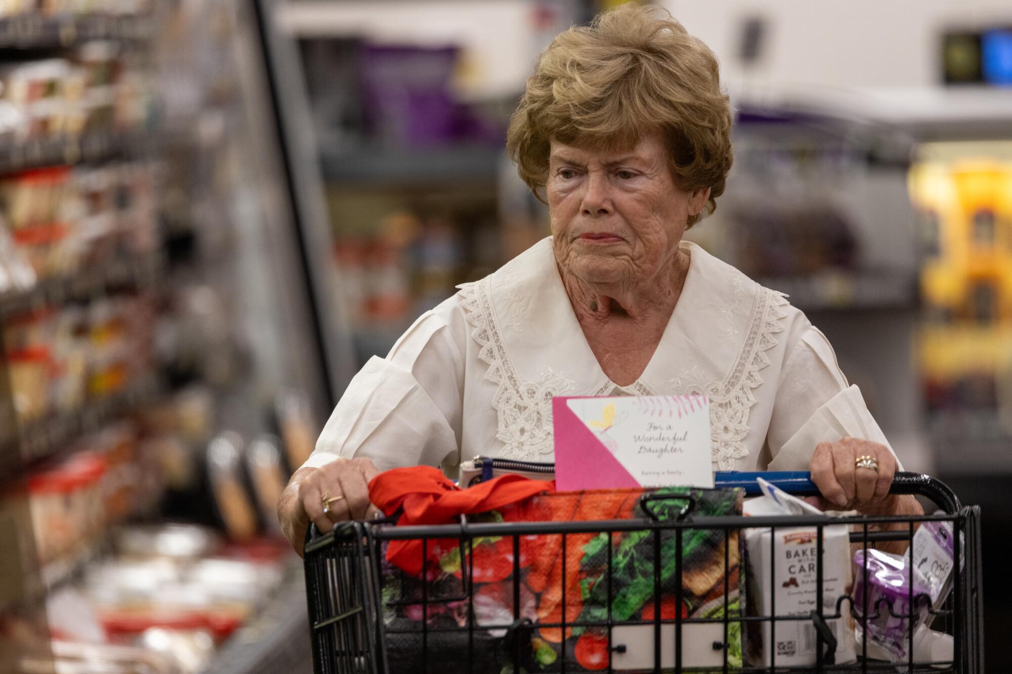 A woman pushes a shopping cart in a grocery store.