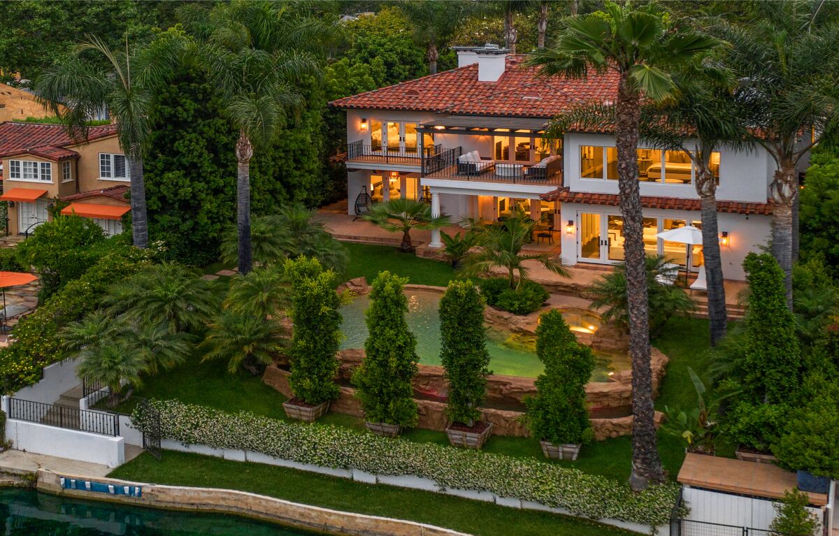 A view of the home's exterior, with two stories, multiple windows, balcony, patio and pool surrounded by rock.