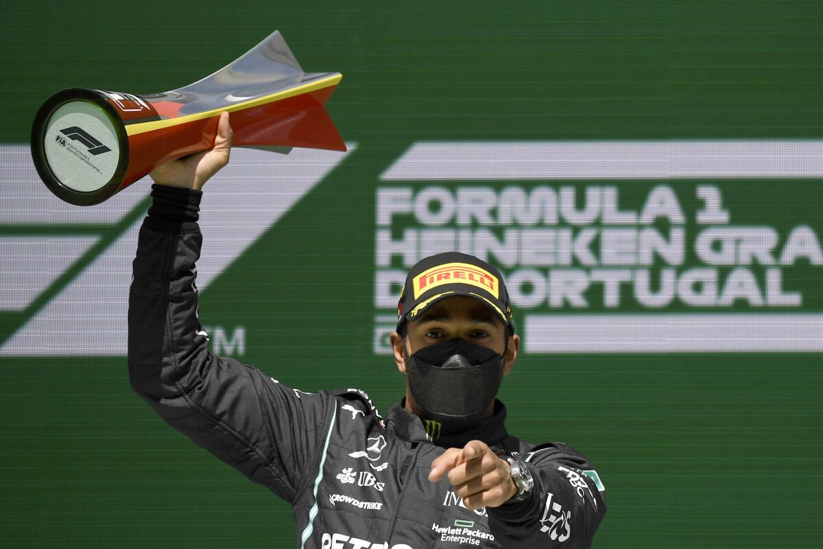 Lewis Hamilton holds up a trophy and points straight ahead after winning the Portugal Formula One Grand Prix.