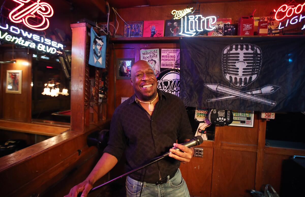 A smiling man holds a microphone inside a bar 