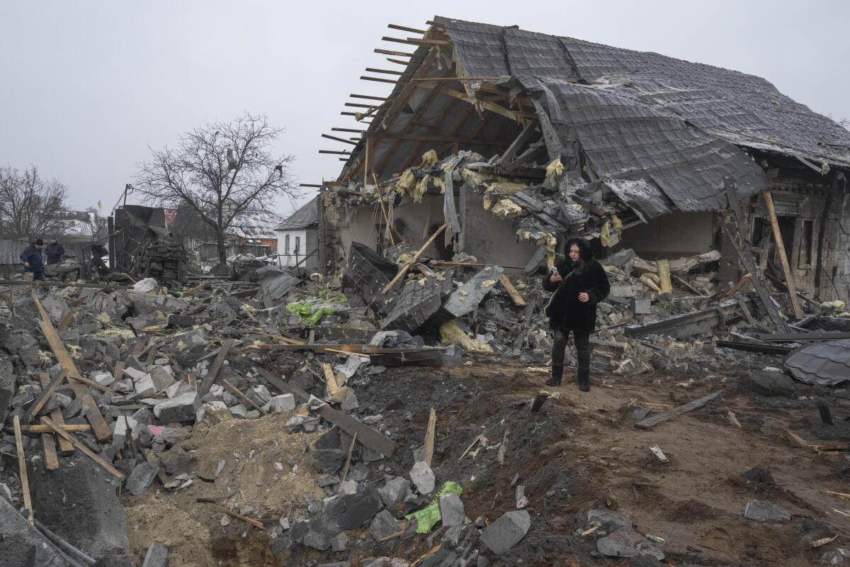 A person stands next to a debris crater and destroyed house.