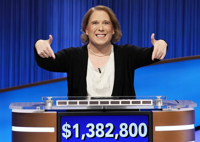 A woman standing behind a podium, smiling and pointing to a blue screen that says "$1,382,800"