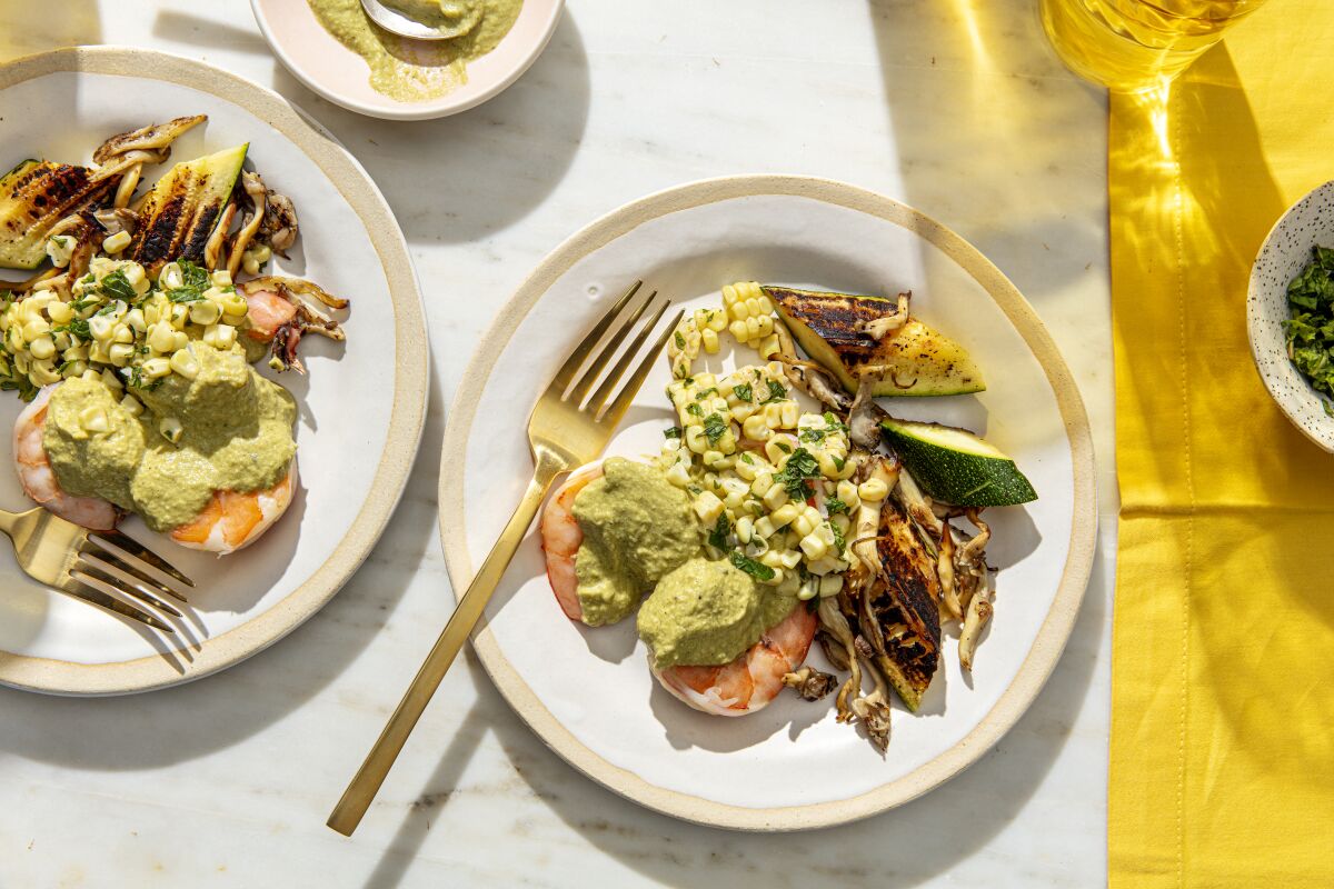 Two white dishes served with shrimp, corn and zucchini, topped with green sauce.