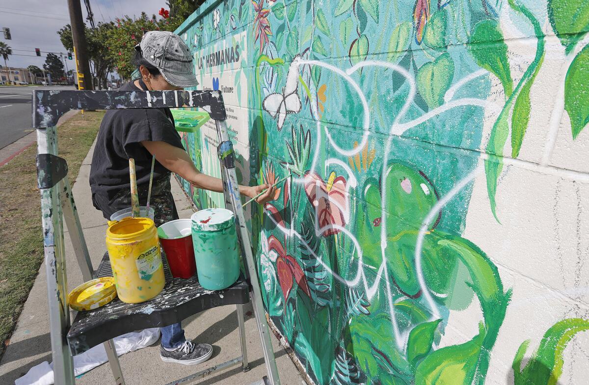Artist Maria Angeles Soto carefully paints over vandalism Tuesday on a "Poderosas" mural  on Costa Mesa's Baker Street.