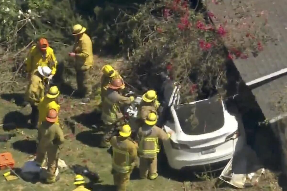 Firefighters surround a white Tesla car crashed into landscaping in a yard outside a home