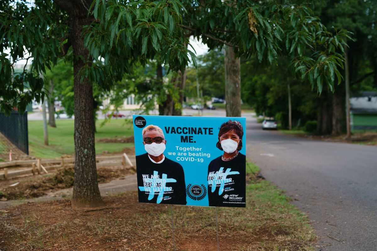 A roadside sign beneath trees, says "Vaccinate me. Together we are beating COVID-19."