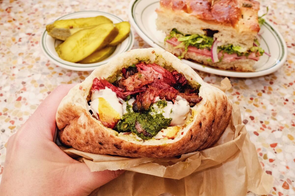 A hand holds pita stuffed with lamb, brisket and sauce at Saffy's in East Hollywood. A sandwich and pickles in the background