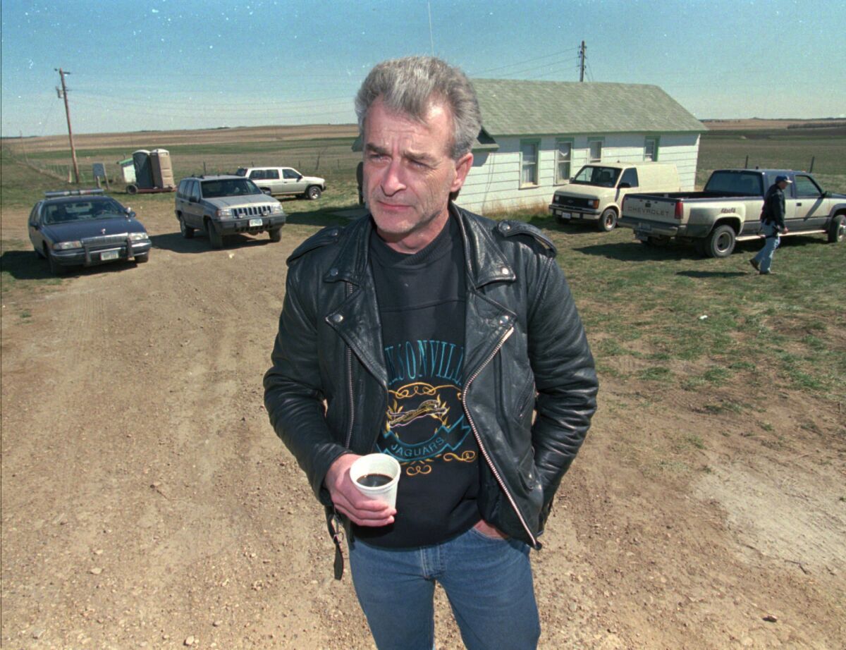 Randy Weaver holds a beverage while standing outside near several vehicles