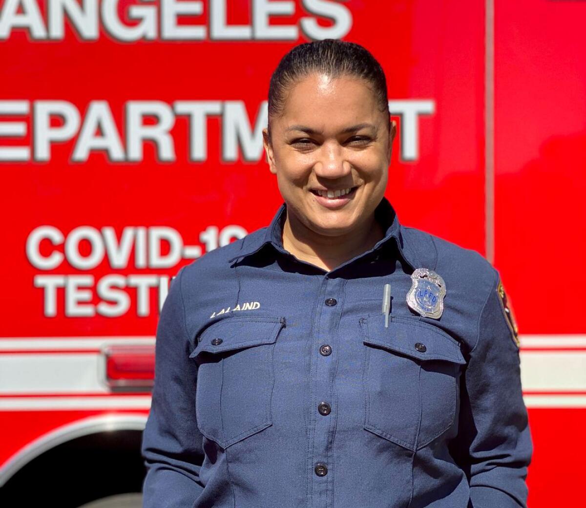 A woman in a firefighter's uniform stands before a red firetruck