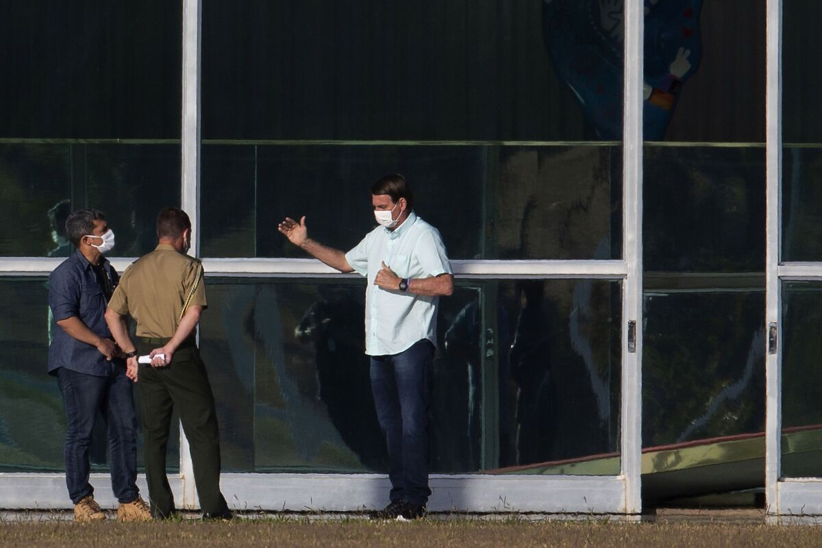 Brazil's President Jair Bolsonaro, center right, wearing a protective face mask, talks with staff outside his official residence Alvorada Palace, in Brasilia, Brazil, Tuesday, July 14, 2020. Last week, Bolsonaro announced that he has tested positive for the new coronavirus, making him one of the more than 1.6 million Brazilians with confirmed infections. (AP Photo/Eraldo Peres)