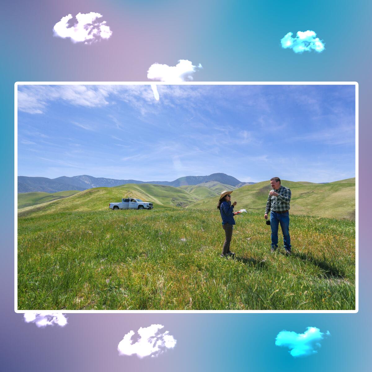A man and a woman stand in a meadow with hills in the background.