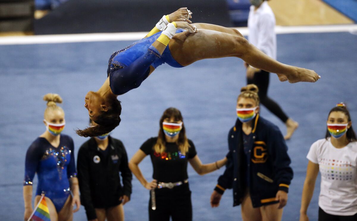 A gymnast dismounts as people spectate