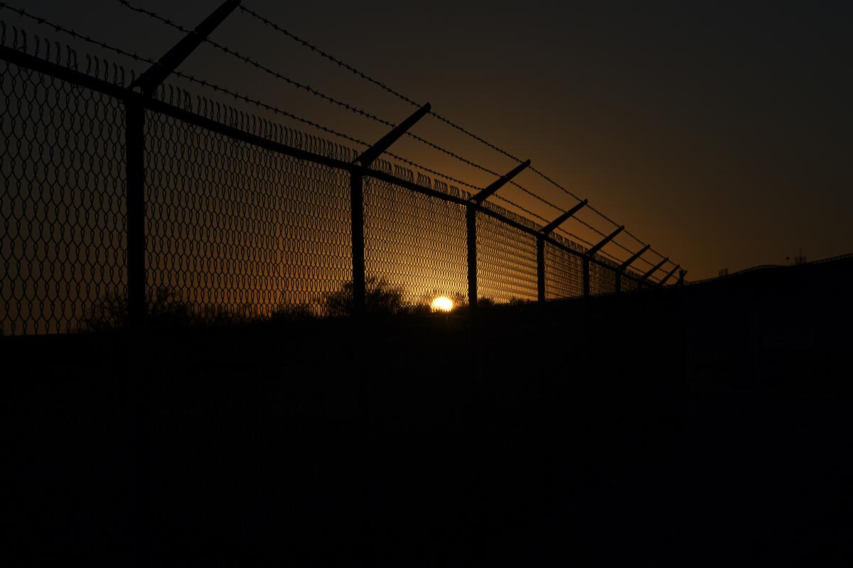 The sun sets behind a border fence