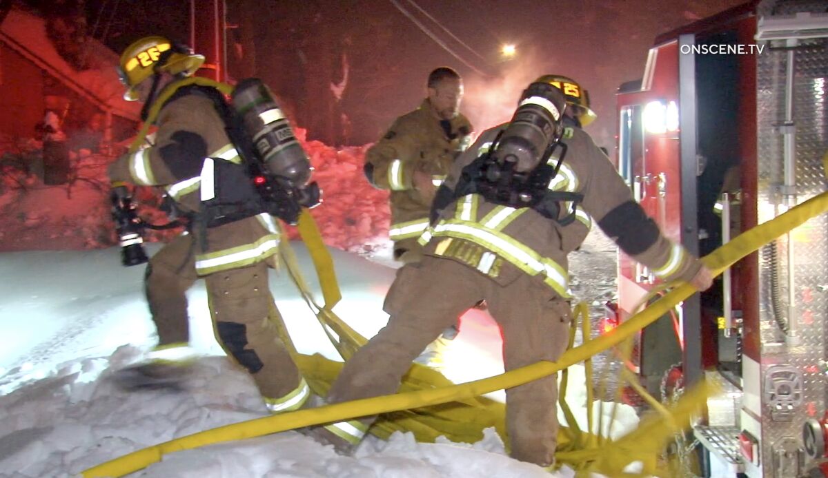 Firefighters pull hose from a fire engine in the snow at night