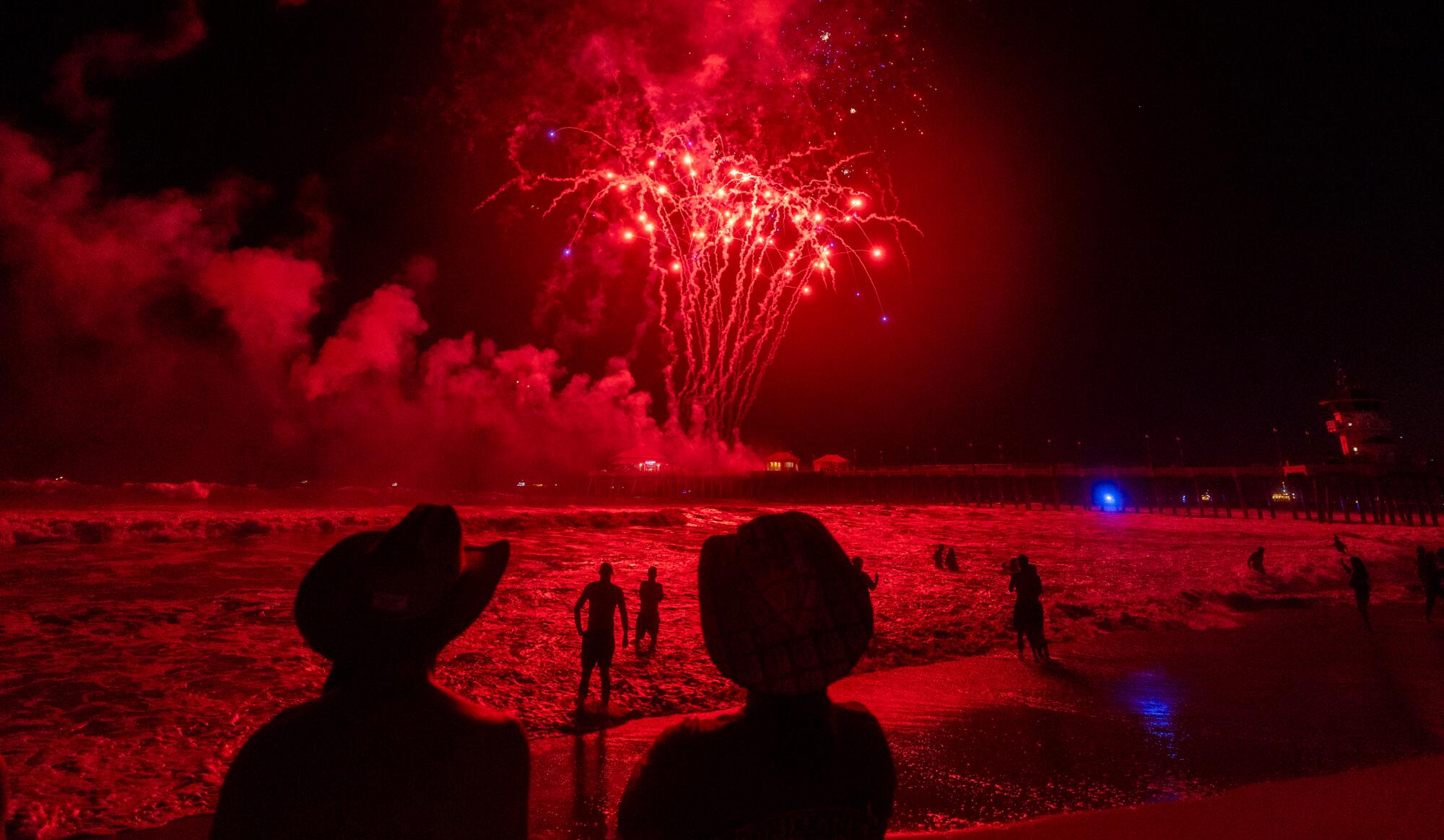 Two people watch the sky light up with fireworks over Huntington Beach.