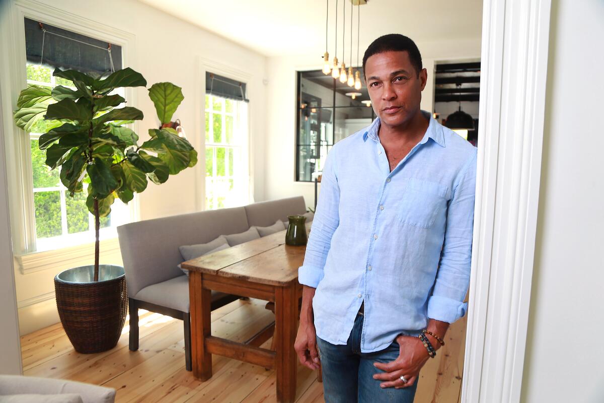 Don Lemon leans against a door jamb in a modern-looking room with a large potted ficus