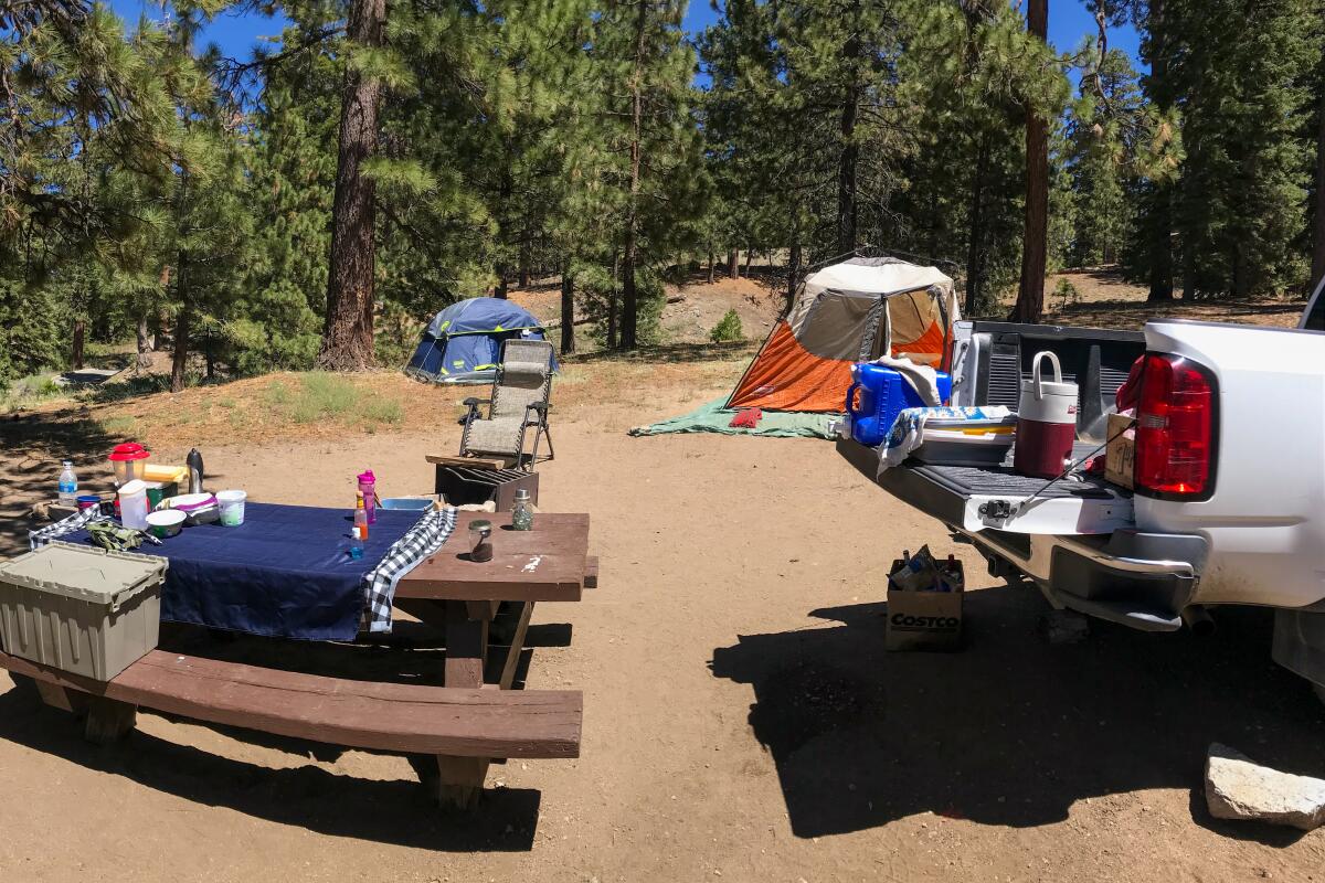 A campsite with a brown picnic table and truck bed in the foreground and orange tent the background