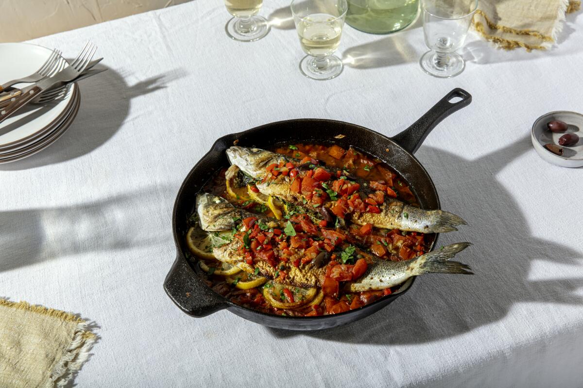 A dish of roasted branzino with tomatoes and olives.