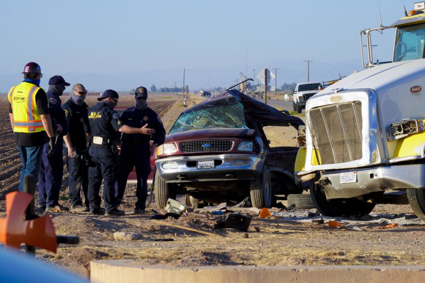 Holtville, CA - March 02: On Tuesday, March 2, 2021 in Holtville, CA., law enforcement investigator look over the SUV after tow wreckers separated it from the and large tractor trailer. The accident was the scene of a deadly crash on State Highway115 near the U.S.-Mexico border. The crash Tuesday morning left at least 13 people dead and several others injured. (Nelvin C. Cepeda / The San Diego Union-Tribune)