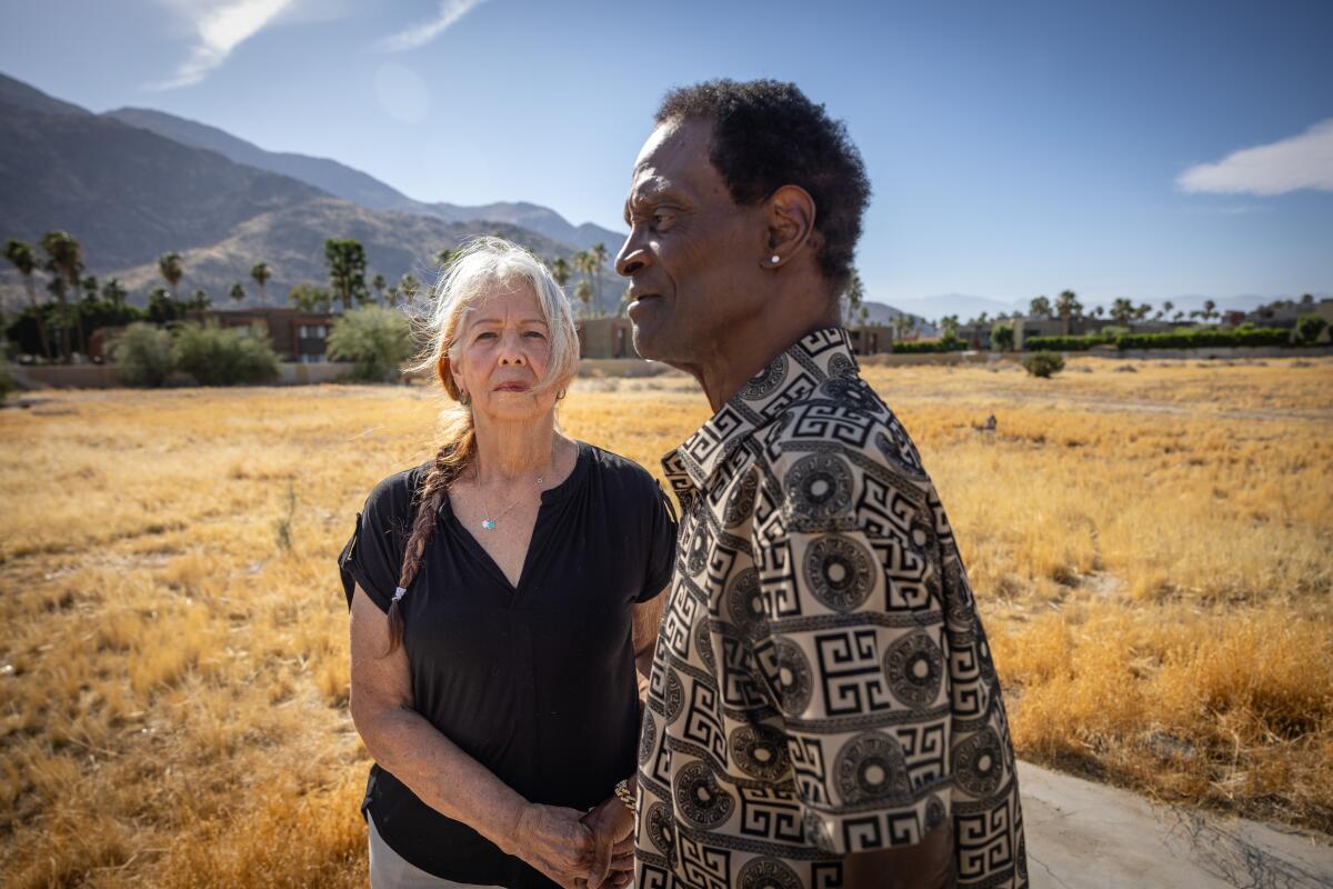 A man and woman stand in a dry field