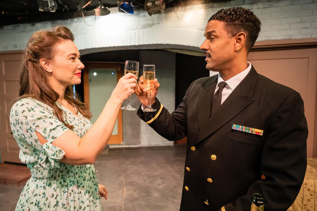 Austin Highsmith Garces, in a print dress, and C.J. Lindsey, in a naval uniform, clink champagne in a scene from "Home Front"