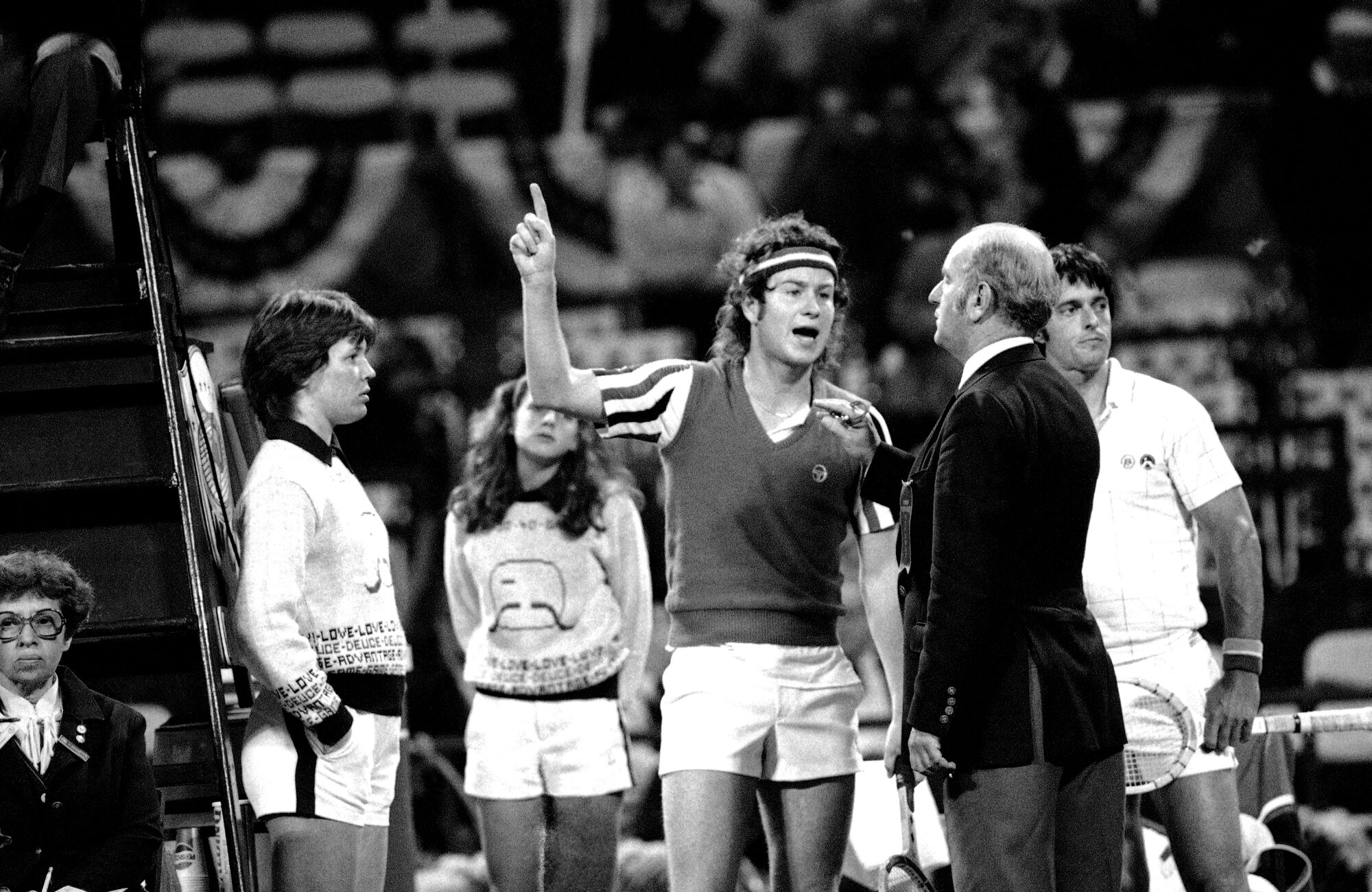 In a May 9, 1980, photo, John McEnroe points to the sky as he argues a call with an umpire and the head referee. 