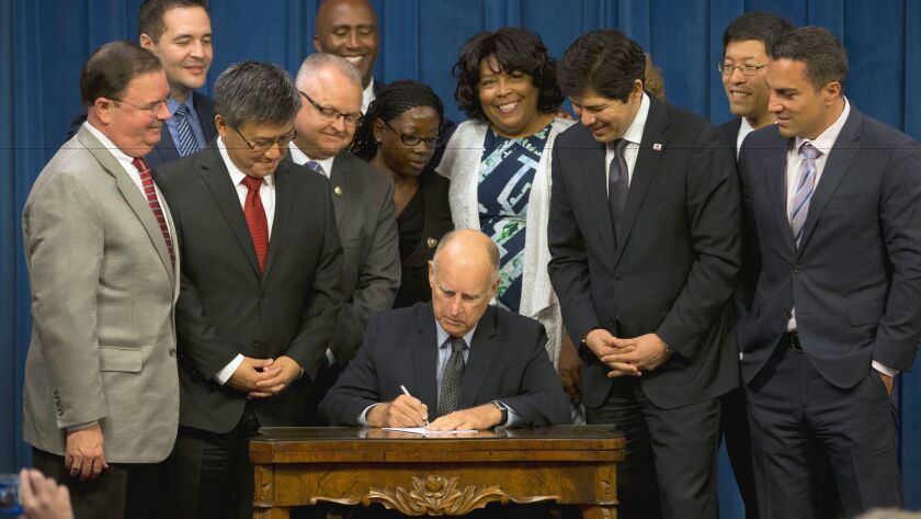 As lawmakers and supporters look on, Gov. Jerry Brown signs legislation that will automatically enroll millions of private-sector workers in retirement saving accounts.