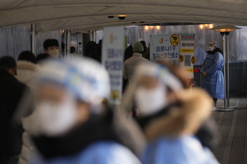 Health workers wearing protective gears stand to help visitors at a temporary screening clinic for the coronavirus near the Seoul City Hall in Seoul, South Korea, Wednesday, Jan. 26, 2022. (AP Photo/Lee Jin-man)