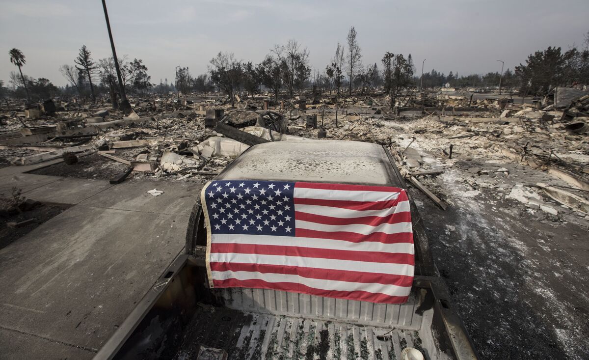 An American flag adorns a burned-out pickup truck in Santa Rosa, where fierce, dry winds whipped the Tubbs fire — one of 17 burning in the state — through residential areas.