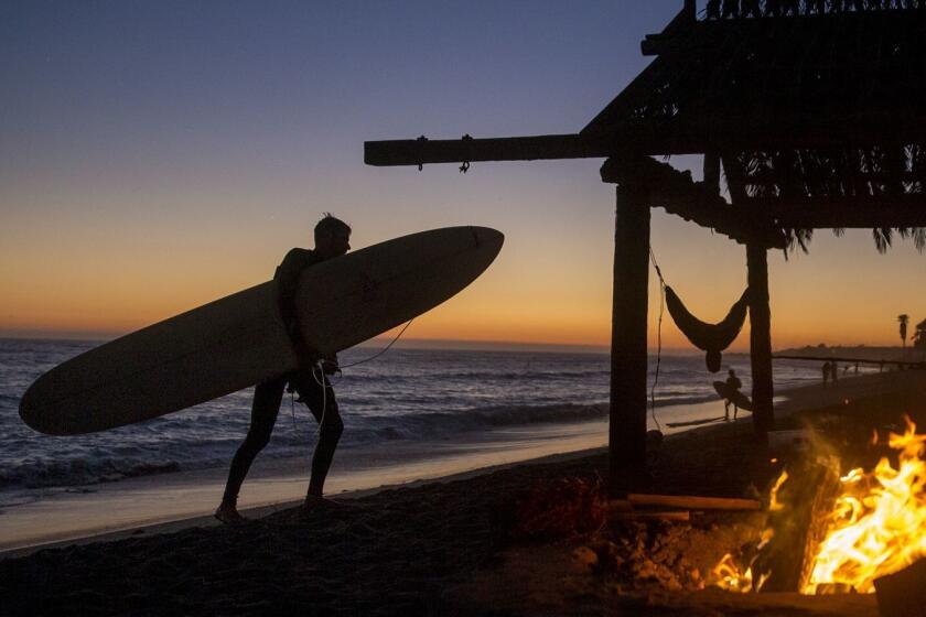 SAN CLEMENT, CA -- TUESDAY, AUGUST 16, 2016: A surfer heads in by a fire pit, hammock and palapa at dusk at "old man's" section of San-O, or San Onofre State Beach in San Clemente. San Onofre was leased to the state by the United States Marine Corps in 1971. San Onofre has a longtime history as a surfer's favorite with it's consistent waves and the evolution of Southern Californiaâs modern surf culture. (Allen J. Schaben / Los Angeles Times)