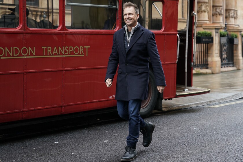 A man in a coat walks past a London Transport bus.