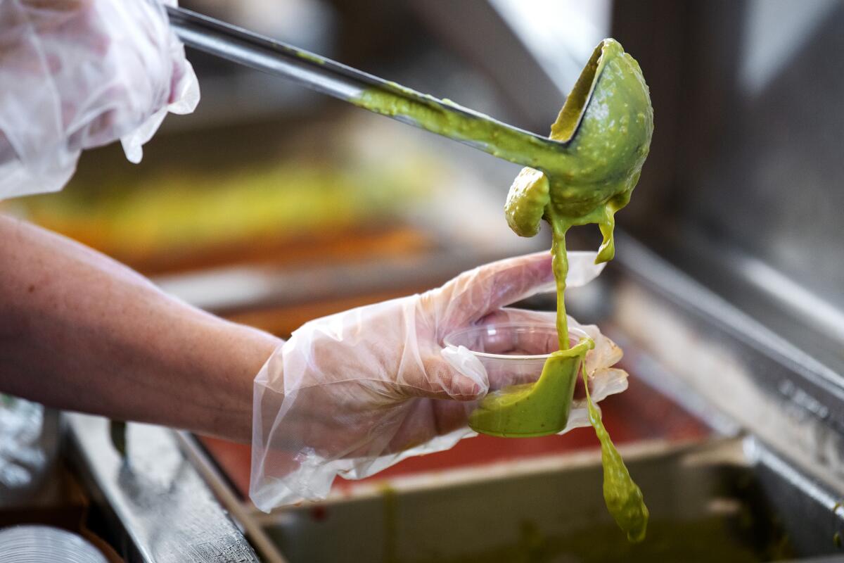 A Tito's Tacos employee scoops guacamole into a container.