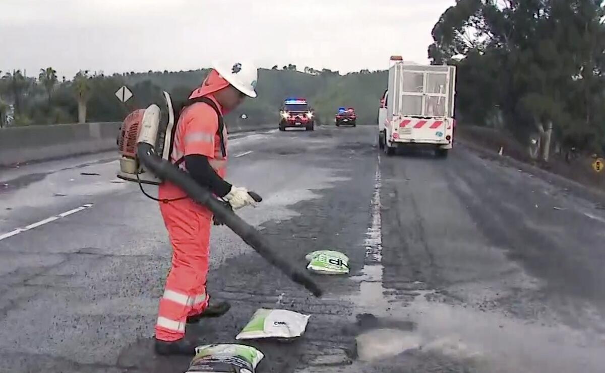 A Caltrans worker stands on a closed roadway with equipment strapped to his back while working on a pothole.