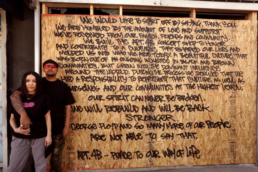 LOS ANGELES, CA - JUNE 01, 2020 - - Moon Moronta, right, and his wife Monique, stand in front of their store APT.4B that is now boarded up after being looted last Saturday along Fairfax Ave. in the Fairfax District in Los Angeles on Monday, June 1, 2020. "Our spirit can never be broken," says a portion of their statement to Los Angeles that was spray painted on their boarded up storefront by Josh Geisler. The Moronta's wrote the statement of thanks and perseverance. (Genaro Molina / Los Angeles Times)