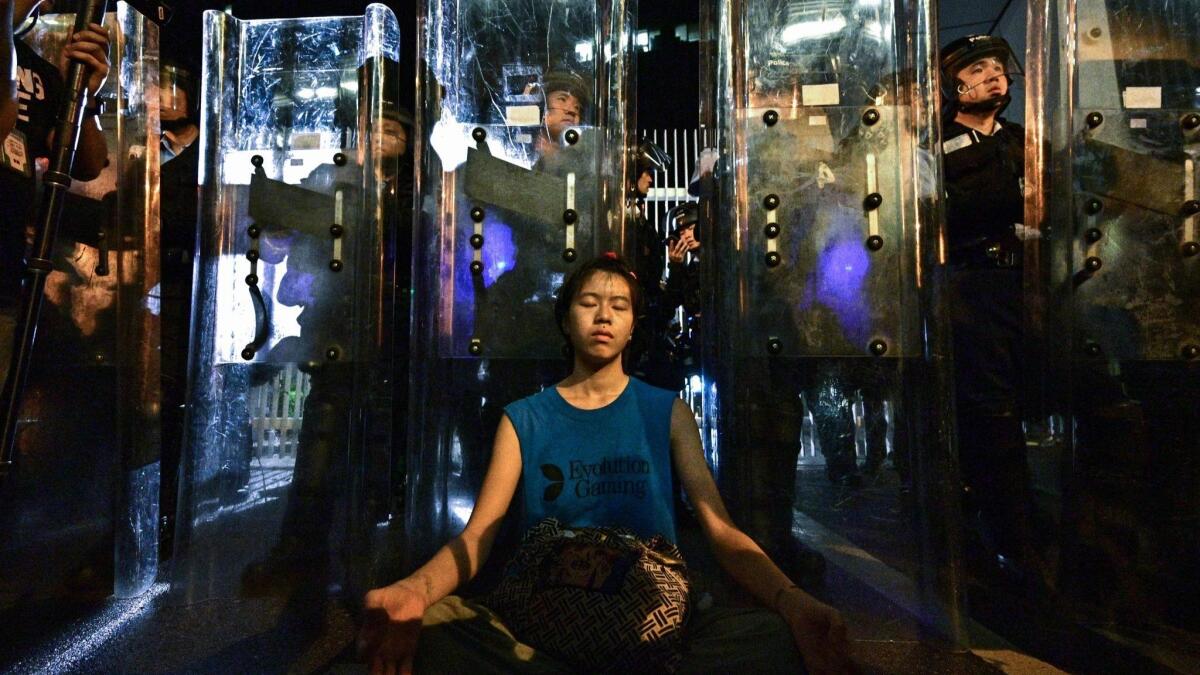 A woman meditates in front of a line of riot police standing guard outside the government headquarters in Hong Kong.